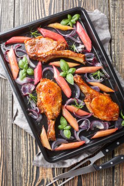 Kızarmış domuz bifteği, kırmızı soğanlı pirzola, masadaki fırın tepsisine yakın plan otlar ve ravent. Yukarıdan dikey üst görünüm