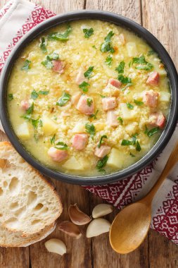 Çorba kulesh darı, patates ve domuz pastırması siyah bir kâse içinde ahşap bir masada yakın plan. Yukarıdan dikey üst görünüm