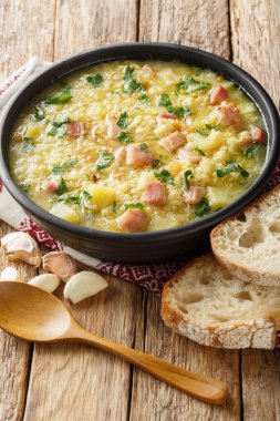 Çorba kulesh darı, patates ve domuz pastırması siyah bir kâse içinde ahşap bir masada yakın plan. Dikey