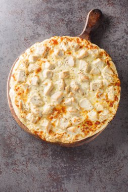 Masanın üstündeki ahşap tahtaya üzerinde tavuk, mozzarella ve parmesan peyniri olan kremalı ev yapımı alfredo soslu pizza. Yukarıdan dikey üst görünüm