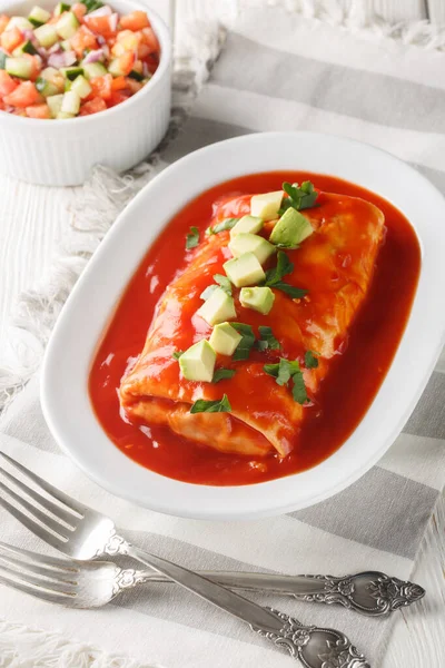 Wet Burrito stuffed with shredded meat, beans, rice and cheese, smothered in red enchilada sauce closeup on the plate on the wooden table. Vertica