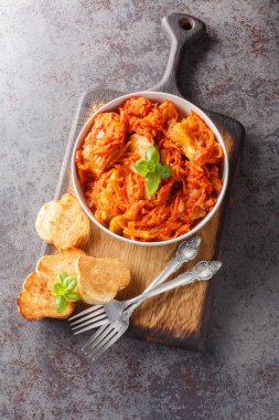 Domates soslu sebzelerle pişirilmiş beyaz deniz balığı parçaları masanın üzerindeki tahta tahtada yakın plan tost ile servis edilir. Yukarıdan dikey üst görünüm