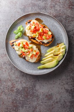 Eritilmiş peynirli ızgara tavuk göğsü, dilimlenmiş avokado ve domatesler masanın üstünde yakın plan. Yukarıdan dikey üst görünüm