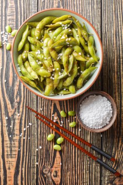 Masadaki tabakta yakın plan deniz tuzu ile baharatlı kavrulmuş edamame fasulyesi. Yukarıdan dikey üst görünüm