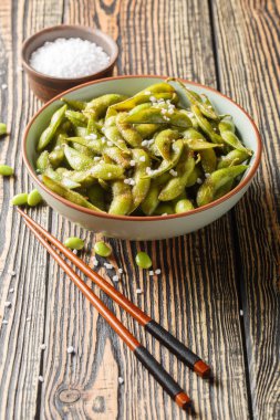 Masadaki tabakta yakın plan deniz tuzu ile baharatlı kavrulmuş edamame fasulyesi. Dikey