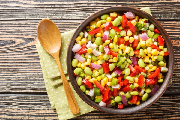 Vitamin salad of summer vegetables with edamame soybeans, bell peppers, corn, tomatoes and onions close-up in a bowl on the table. Horizontal top view from abov