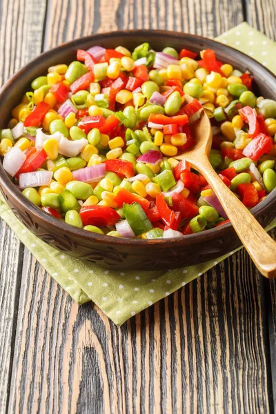 Vegetable salad with edamame beans, bell peppers, corn, tomatoes and onions close-up in a bowl on the table. Vertica