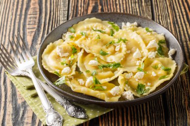 Yumuşak keçi peyniri ile doldurulmuş hilal mezzaluna makarnası ve masada yakın plan otlar. Yatay