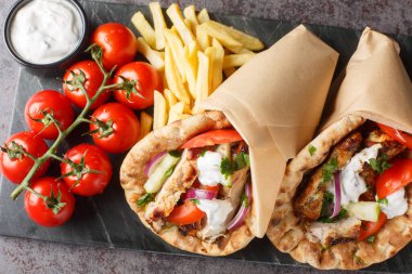 Tavuklu, domatesli, salatalıklı ve soğanlı Yunan fast food jiroskopu, masada tzatziki sosu ve patates kızartmasıyla servis ediliyor. Yukarıdan yatay üst görünüm