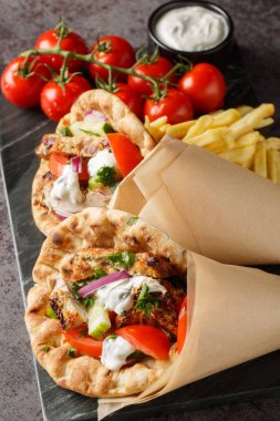 Tavuklu Yunan jiroskopları ve taze sebzelerle servis edilen tzatziki sosu ve masada yakın plan patates kızartması. Dikey