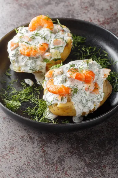 Delicious jacket potatoes with sour cream sauce, dill and shrimp close-up in a plate on the table. Vertica