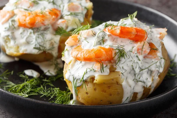 Hot jacket potatoes topped with sour cream sauce, dill and shrimp close-up in a plate on the table. Horizonta