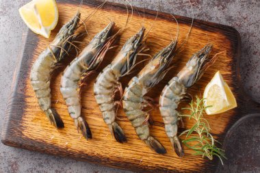 Soyulmamış siyah kaplan karidesleri, limonlu karidesler ve masadaki ahşap tahtaya yakın plan biberiye. Yukarıdan yatay üst görünüm