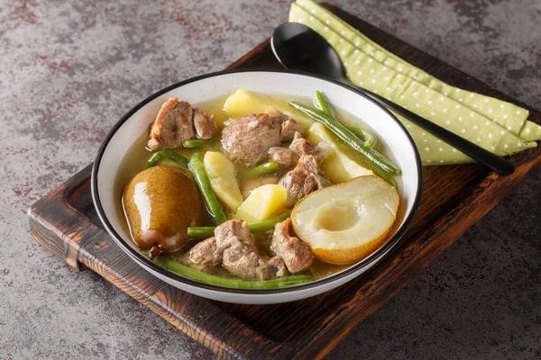 Lamb stew with pears, potatoes, green beans in a spicy sauce close-up in a bowl on a wooden board. horizonta