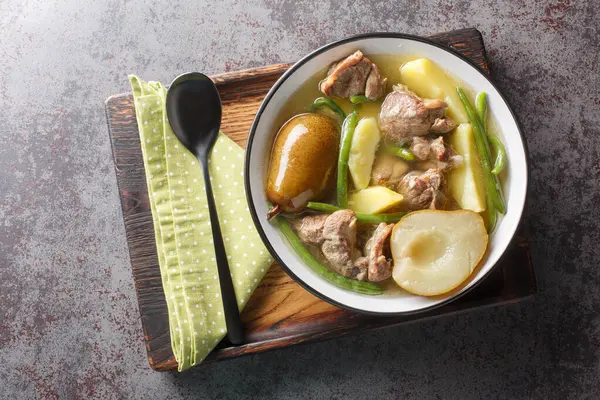 Swedish Lamb stew with fresh pears, potatoes, green beans close-up in a bowl on a wooden board. horizontal top view from abov