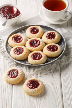 Beyaz ahşap masada çay ile servis edilen tabağa ahududu reçeli ile doldurulmuş parmak izi Noel kurabiyeleri. Dikey