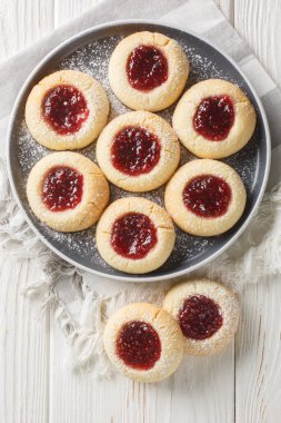 Klasik parmak izli kurabiyeler basit bir şekerli kurabiye hamuruyla yapılır ve sonra da ahududu reçeli ile doldurulur beyaz ahşap masadaki tabağa yakın plan. Yukarıdan dikey üst görünüm