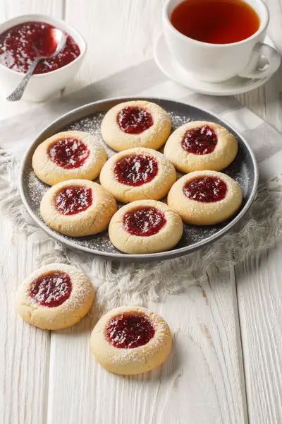 Thumbprint Christmas cookies filled with raspberry jam closeup on the plate served with tea on the white wooden table. Vertica