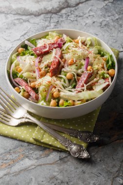 Lezzetli dengeli nohut salamı salatası, buzdağı ve romaine marulu, mozzarella, soğan yakın plan masa üstünde. Dikey