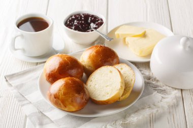 Norveç Boller veya Hveteboller çörekleri tereyağı, reçel ve kahve eşliğinde ahşap masada servis edilir. Yatay