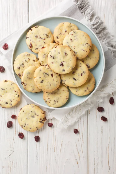Cranberry orange shortbread cookies are bursting with flavour from dried cranberries and fresh orange zest closeup on the plate on the wooden table. Vertical top view from abov