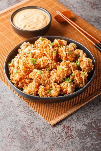 Bang bang chicken is a tender chunks of chicken coated in a crunchy Panko crust, fried to golden and finally smothered in a creamy, sweet and spicy sauce closeup on the plate on the table. Vertica