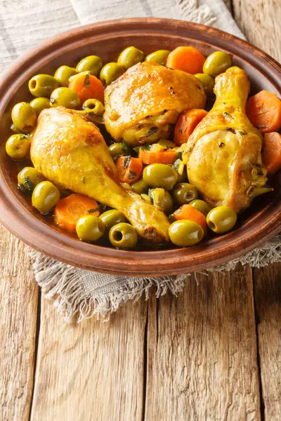 Tajine Zitoune is an Algerian stew dish that consists of chicken cooked with carrots and green olives using north African spices close-up on wooden table. Vertica
