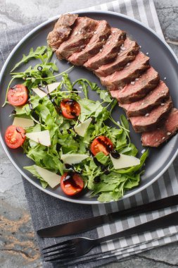 İtalyan biftekli Tagliata salatası, yaban roketi, vişneli domates ve masada yakın plan parmesan peyniri. Yukarıdan dikey üst görünüm