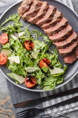 Arugula, parmesan ve vişneli domatesli sığır eti tagliata, masanın üzerindeki bir tabağa sığır etinden yapılmış lezzetli bir ana yemektir. Yukarıdan dikey üst görünüm