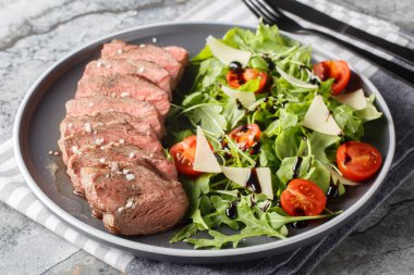 Geleneksel İtalyan ana yemeği biftek, roka, kiraz domatesleri, Grana Padano talaşı, masadaki bir tabağa yakın çekimde balzamik redüksiyon. Yatay