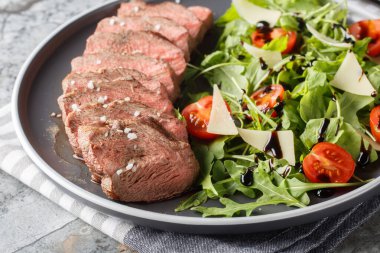 İtalyan biftekli Tagliata salatası, yaban roketi, vişneli domates ve masada yakın plan parmesan peyniri. Yatay