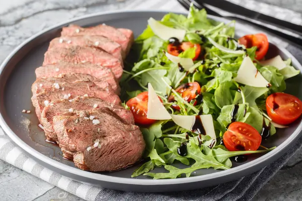 Sliced Seared Steak Tagliata di Manzo served with arugula, cherry tomatoes and parmesan close-up in a plate on the table. Horizonta