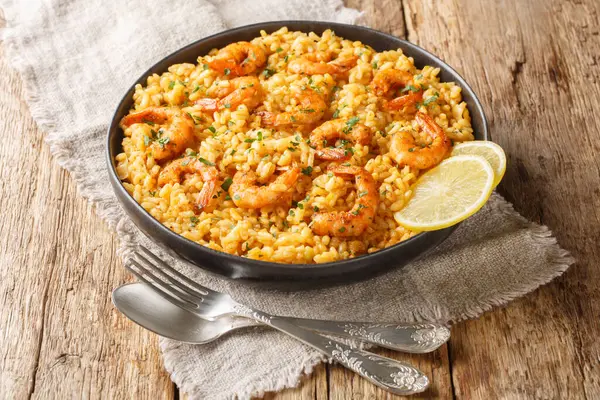 Shrimp risotto is made with fragrant arborio rice sauteed in onions and garlic, simmered stock, and topped with seasoned shrimp closeup on the plate on the wooden table. Horizonta