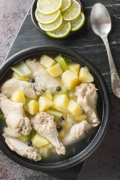 Bahamian chicken souse is a poultry dish made with chicken wings, onions, potatoes, celery, lime juice, allspice closeup on the plate on the table. Vertical top view from abov