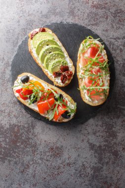 Masanın üzerinde roka, jamon, güneşte kurutulmuş domates, avokado, krem peynir, zeytin ve kavrulmuş biberli taze sandviç. Yukarıdan dikey üst görünüm