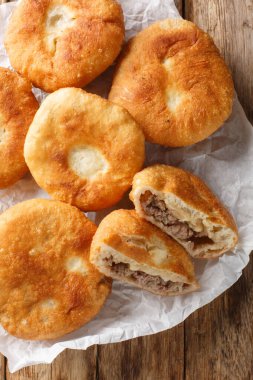 Ev yapımı Rus mutfağı bol yağda kızartılmış belyash hamur hamuru hamur hamuru ve ahşap masadaki kağıdın üzerine et doldurulmuş. Yukarıdan dikey üst görünüm