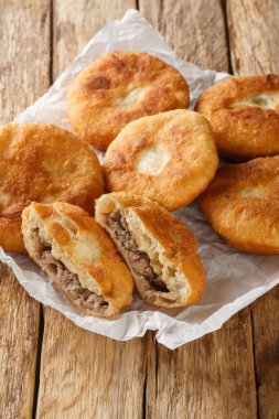 Peremech ya da belyash, ahşap masadaki kağıdın üzerinde eti yakın plan yapılmış bir hamur tatlısı. Dikey