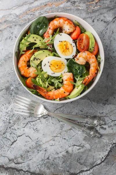 Akdeniz karides salatası, avokado, roka, ıspanak, domates ve haşlanmış yumurtaları masanın üstünde yakın plan. Yukarıdan dikey üst görünüm