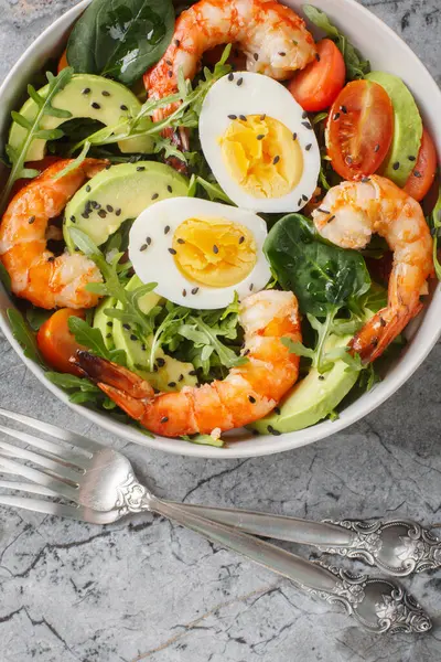 Karides, avokado, roka, ıspanak, domates, susam tohumu ve kaynamış yumurtayla birlikte sağlıklı beslenme salatası. Yukarıdan dikey üst görünüm