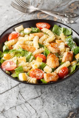 Sezar salatalı fusilli makarna, tavuk, marul, parmesan, domates ve kızarmış ekmekler masanın üstünde. Dikey