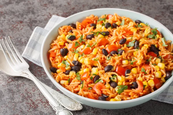Spicy vegetarian side dish tomato rice with black beans, onions and corn close-up in a bowl on the table. Horizonta