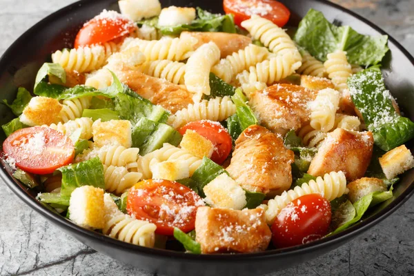 Caesar salad with grilled chicken, pasta, romaine lettuce, parmesan, tomatoes and croutons close-up in a bowl on the table. Horizonta
