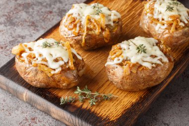 Karamelli soğanla doldurulmuş fırında patates ve masadaki kaseye yakın plan peynir. Yatay