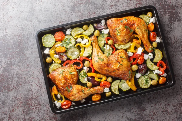 Delicious Mediterranean baked chicken legs with vegetables and feta cheese close-up on a baking sheet on the table. Horizontal top view from abov