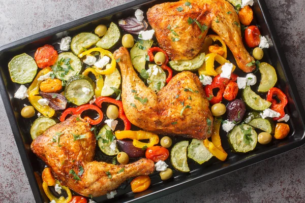 Homemade baked chicken quarters with vegetables and feta cheese close-up on a baking sheet on the table. Horizontal top view from abov