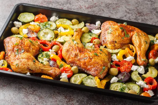 Homemade baked chicken quarters with vegetables and feta cheese close-up on a baking sheet on the table. Horizonta