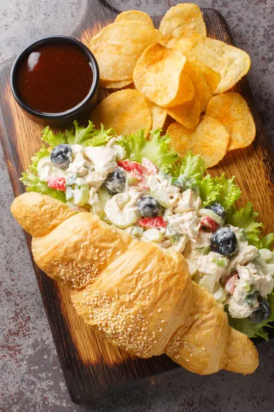 Croissant chicken salad sandwich with potato chips closeup on a wooden board on the table. Vertical top view from abov