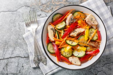 Fırında tavuklu vitamin salatası, taze salatalık, dolmalık biber, havuç ve susam tohumları mermer bir masada yakın plan. Yukarıdan yatay üst görünüm