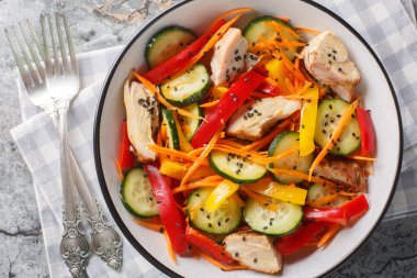 Sağlıklı yiyecek tavuk salatası taze salatalık, dolmalık biber, havuç ve susam tohumları masanın üstünde yakın plan. Yukarıdan yatay üst görünüm