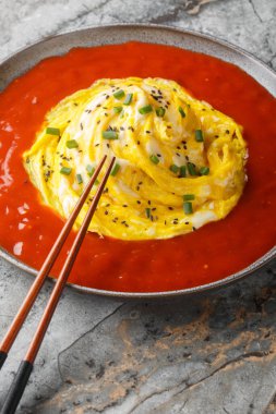 Pirincin üstünde Kore kasırgası omleti ve masanın üzerinde yakın plan bir tabakta acı sos. Dikey